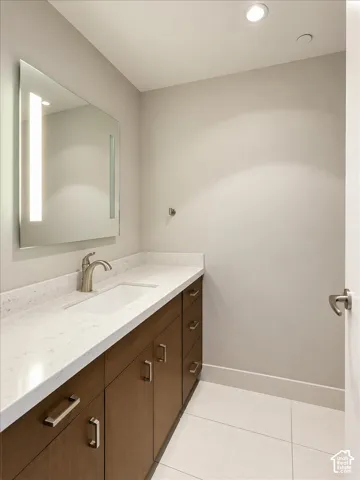Modern vanity featuring wood-finish cabinetry, quartz countertop, integrated rectangular sink, wall-mounted mirror with integrated lighting, and tile flooring