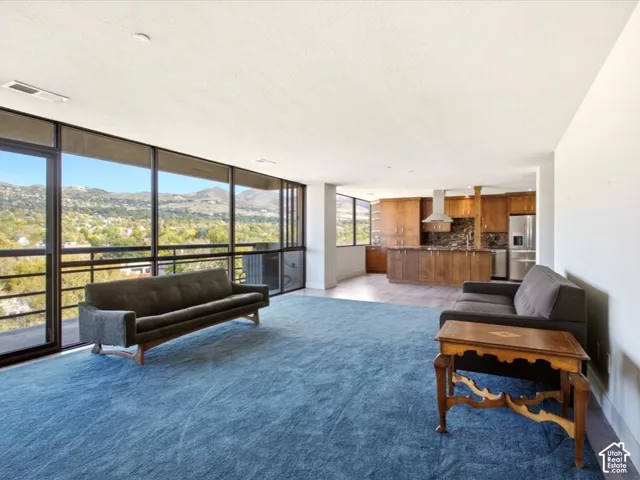 Open-concept floor plan featuring expansive floor-to-ceiling windows with mountain scenery, wood cabinetry, stone-finish countertops, and stainless steel kitchen appliances