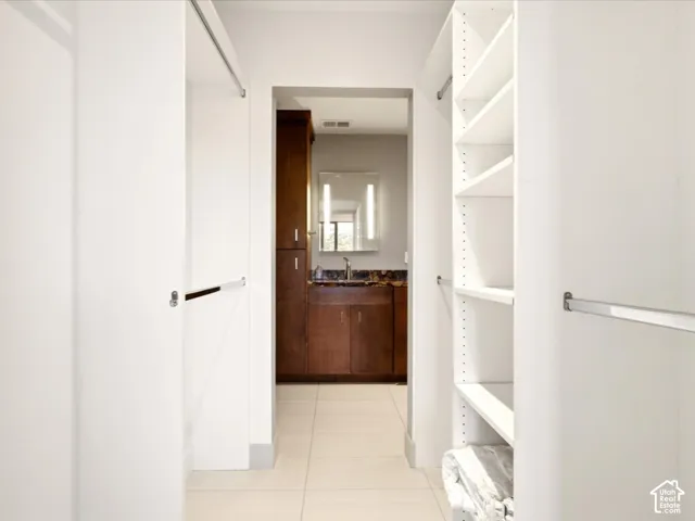 Walk-in closet featuring white built-in shelving and dual hanging rods, ceramic tile flooring, and dark wood cabinetry with a stone countertop