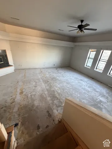High-ceiling room featuring a tiered tray ceiling, three multi-pane windows, a ceiling fan, and a built-in fireplace hearth