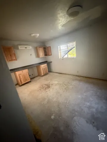 Wood-finish cabinetry, dark countertop, wall-mounted air conditioning unit, and dual flush-mount ceiling lighting