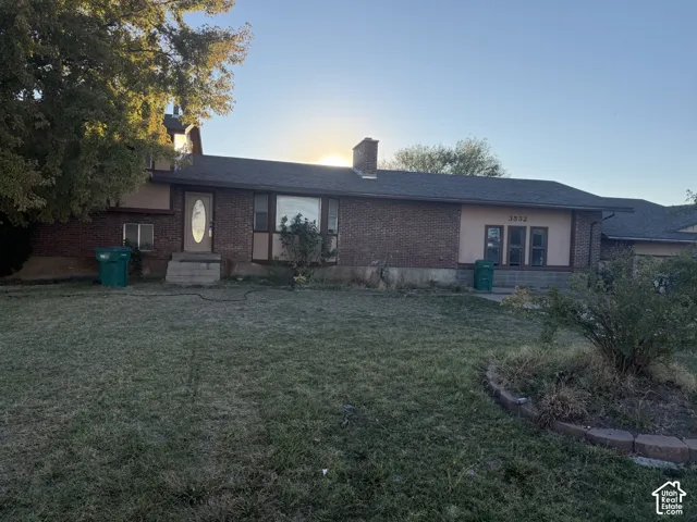 Brick exterior ranch-style home featuring a prominent chimney, large multi-pane windows, and a landscaped front yard with stone-border curbing