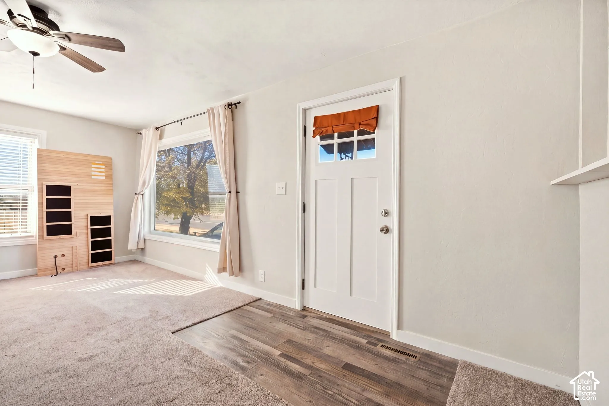 Interior space featuring a white entry door with a six-pane window, large picture window, ceiling fan with light fixture, and wood-finish flooring at the entryway
