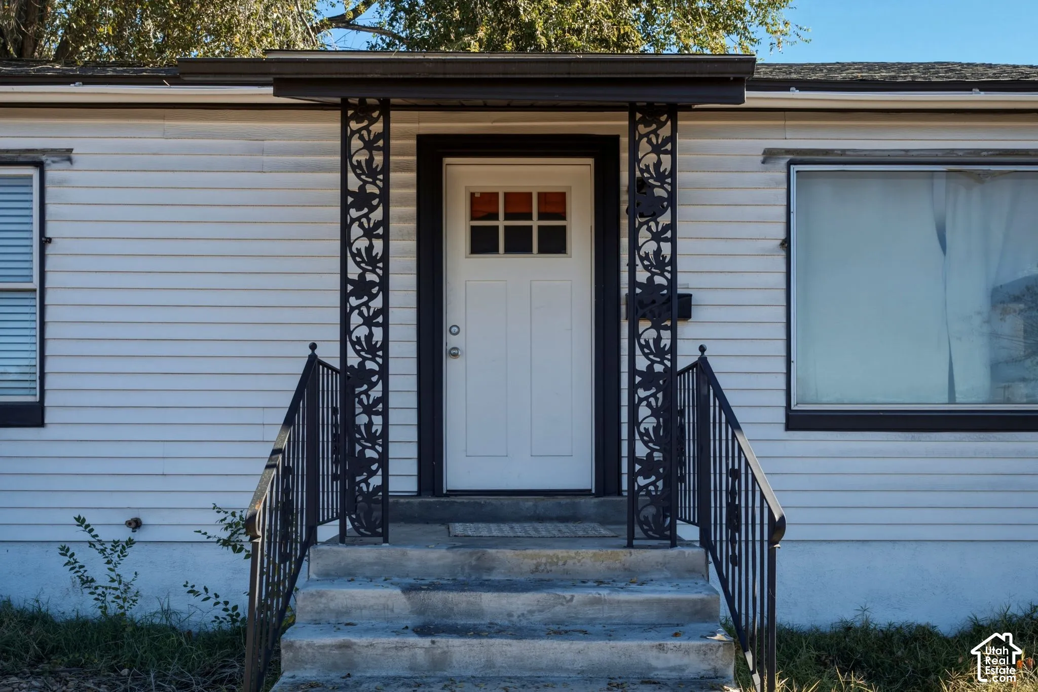 Exterior entry featuring horizontal siding, decorative wrought iron porch supports, concrete steps, metal handrails, and a multi-pane glass-inset door