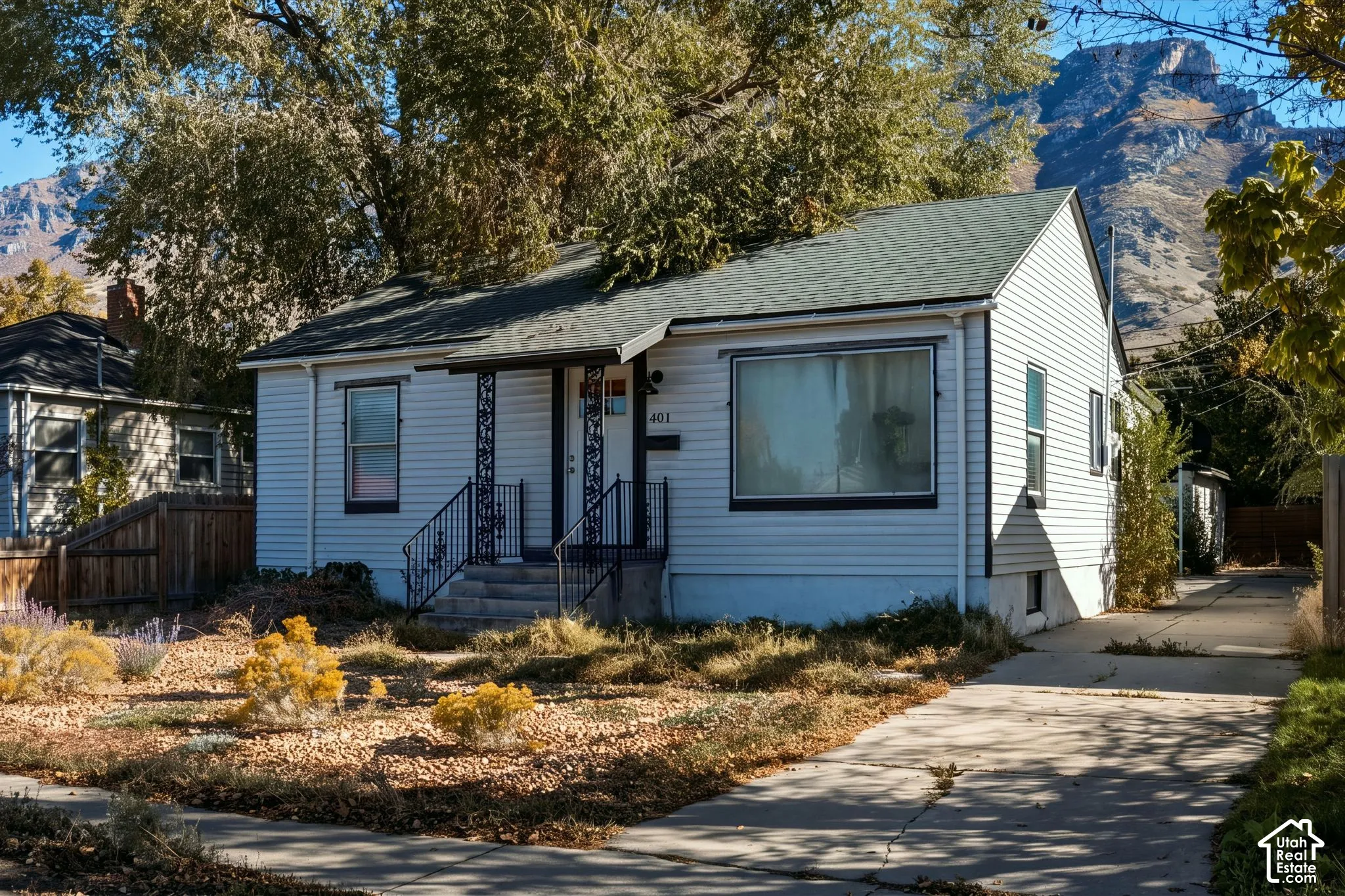 Single-story residence featuring light-colored horizontal siding, decorative wrought-iron porch railings, a concrete driveway, and a mountain backdrop