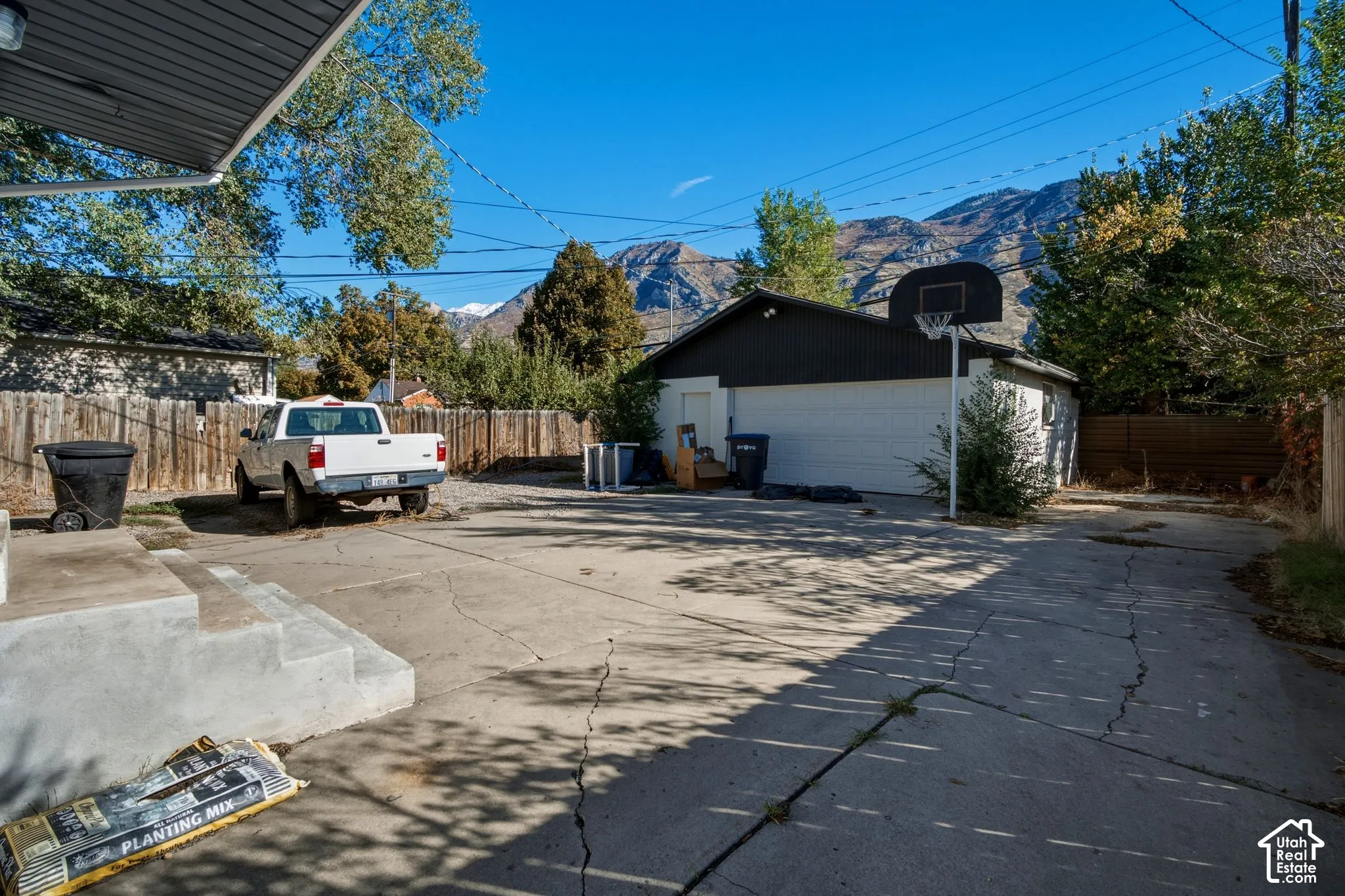 Detached garage with white siding and dark trim, expansive concrete driveway, and prominent mountain backdrop