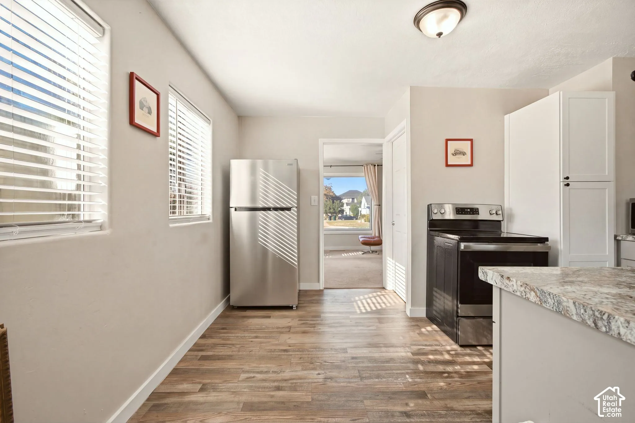 Kitchen area featuring wood-finish flooring, stainless steel refrigerator, black electric range, white cabinetry, and stone-finish countertops