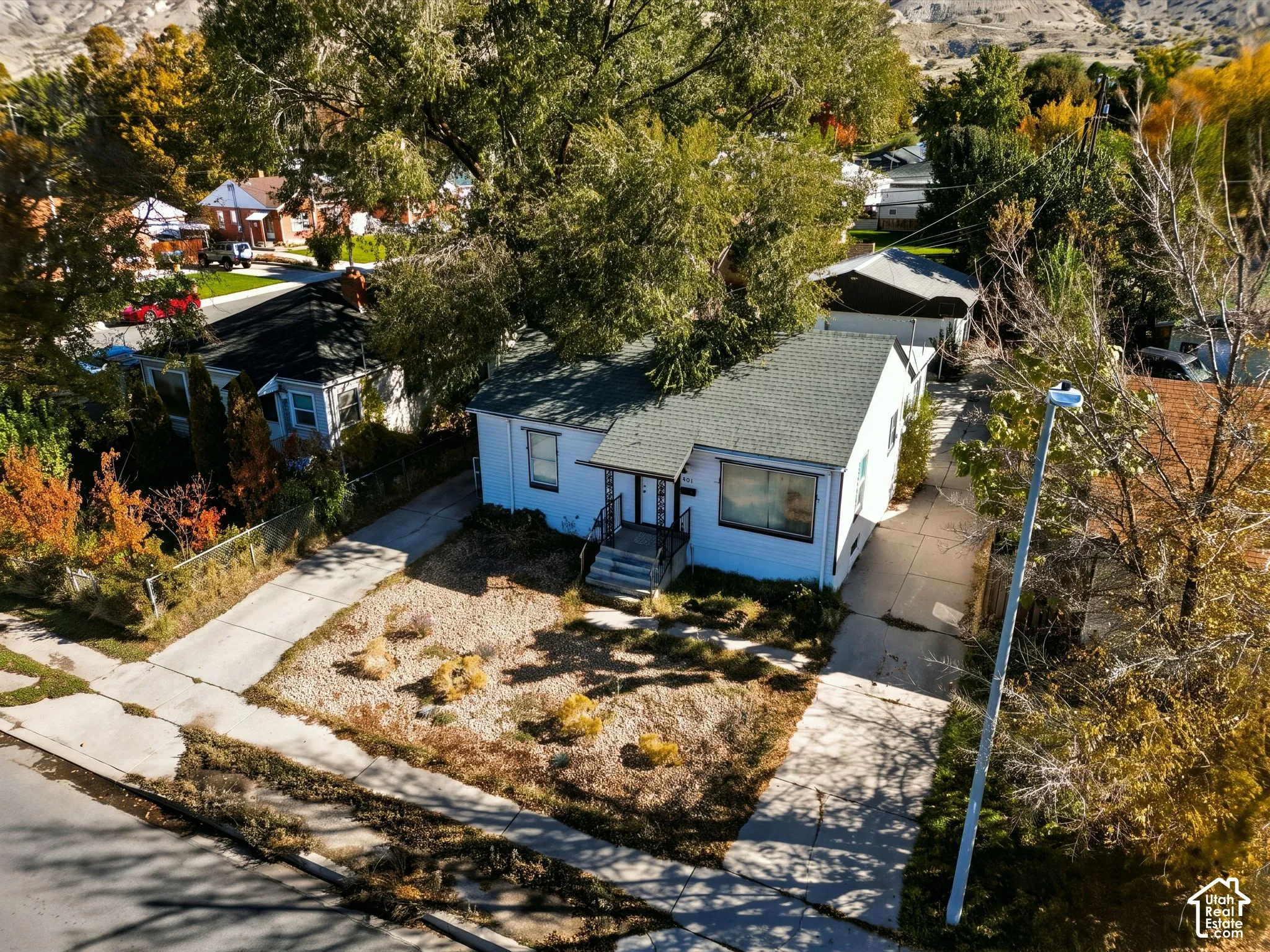 Single-story residence featuring a gabled roofline, concrete driveway, xeriscaped front yard, and an elevated concrete porch with iron railings