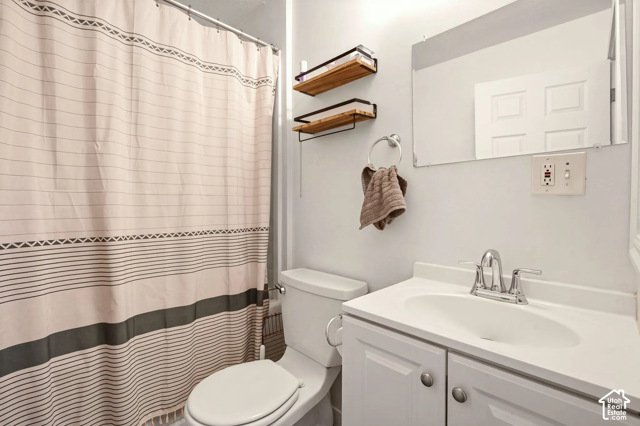Bathroom featuring a vanity with an integrated sink, polished chrome faucet, rectangular frameless mirror, and dual wall-mounted floating shelves