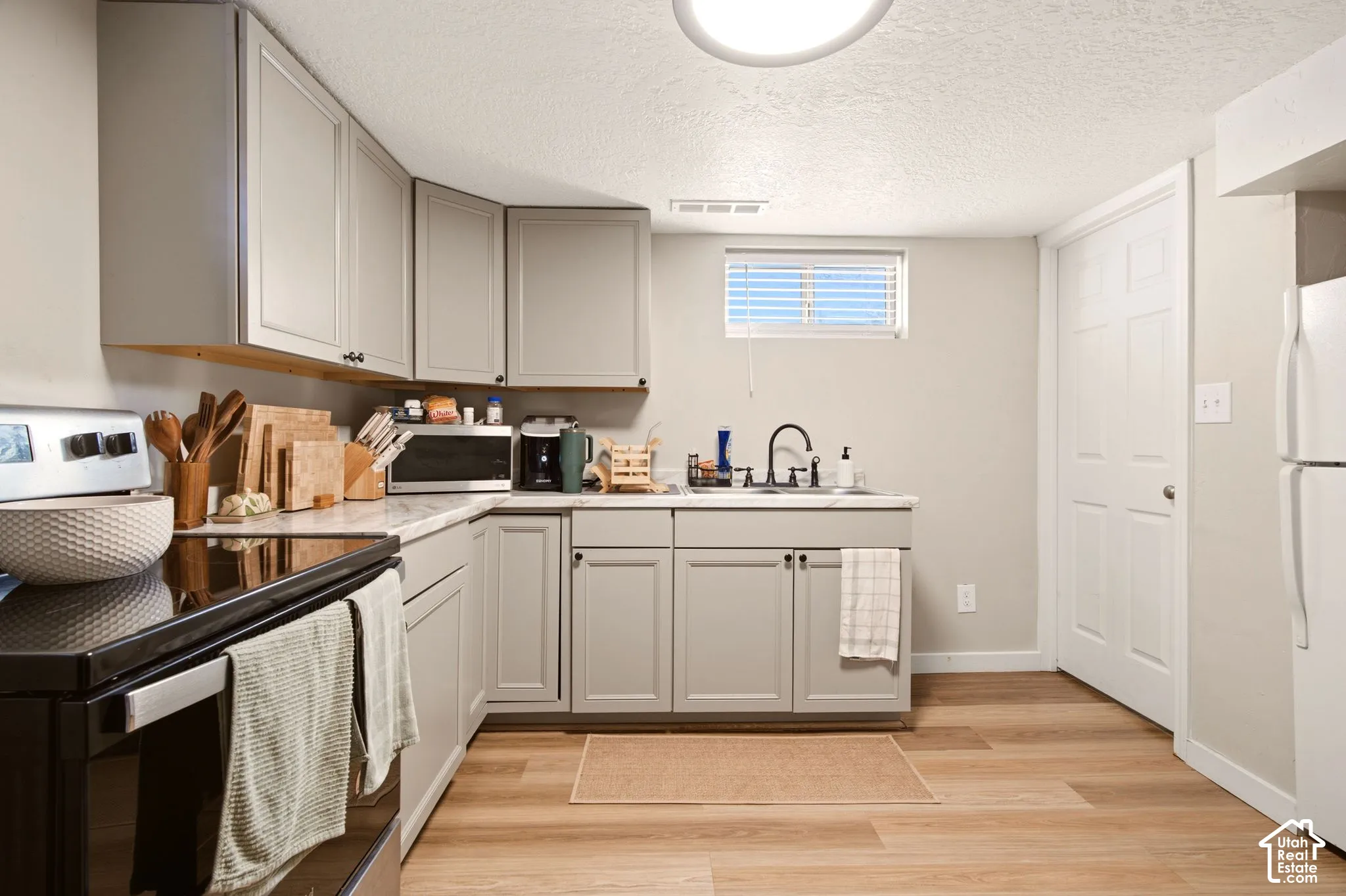 Kitchen featuring gray cabinetry, stone-finish countertops, wood-finish flooring, a double-basin sink with a matte black faucet, and a wall-mounted window