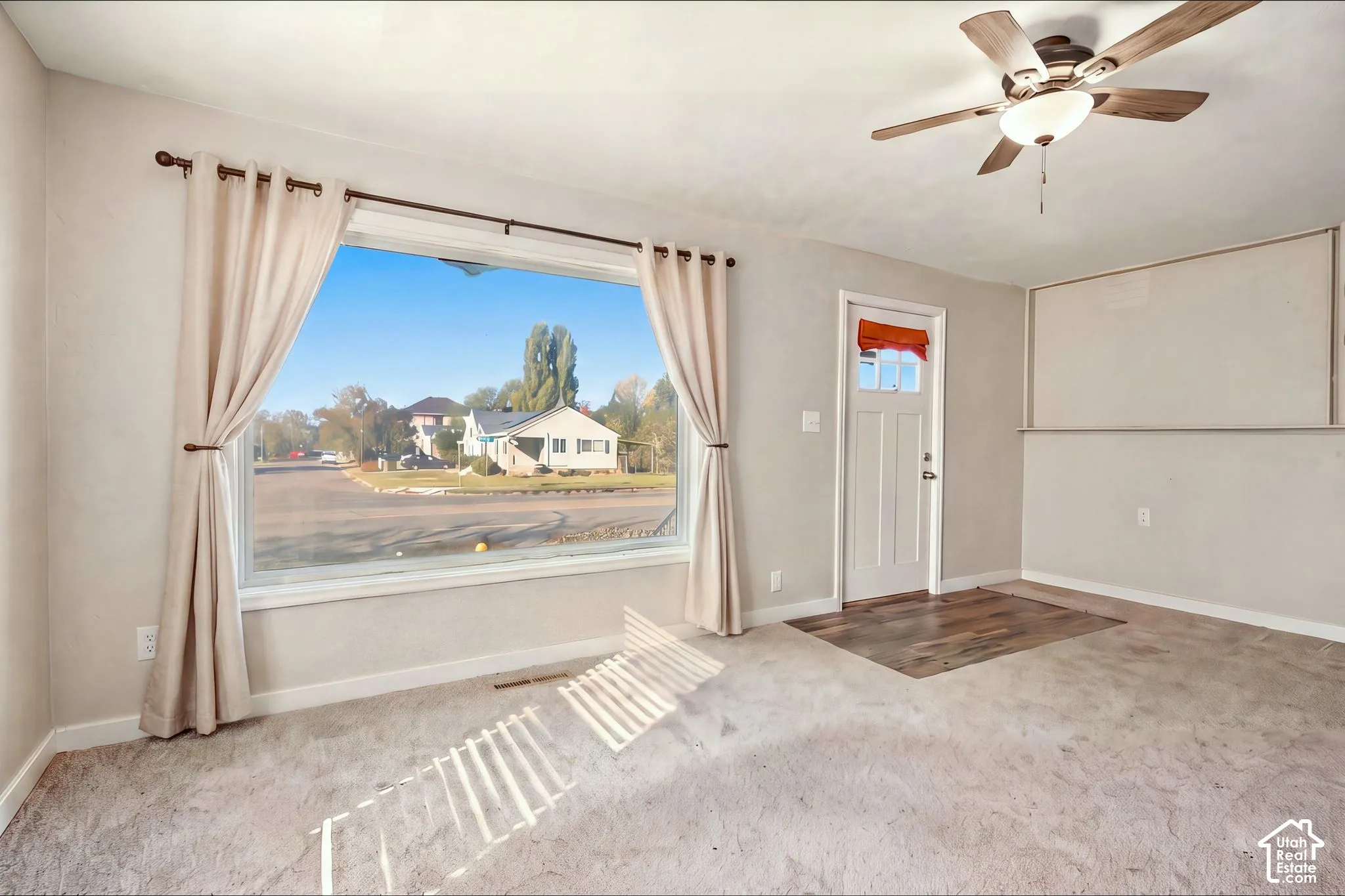 Large picture window, white exterior door with glass pane, ceiling fan with light fixture, and wood-finish flooring entry inlay
