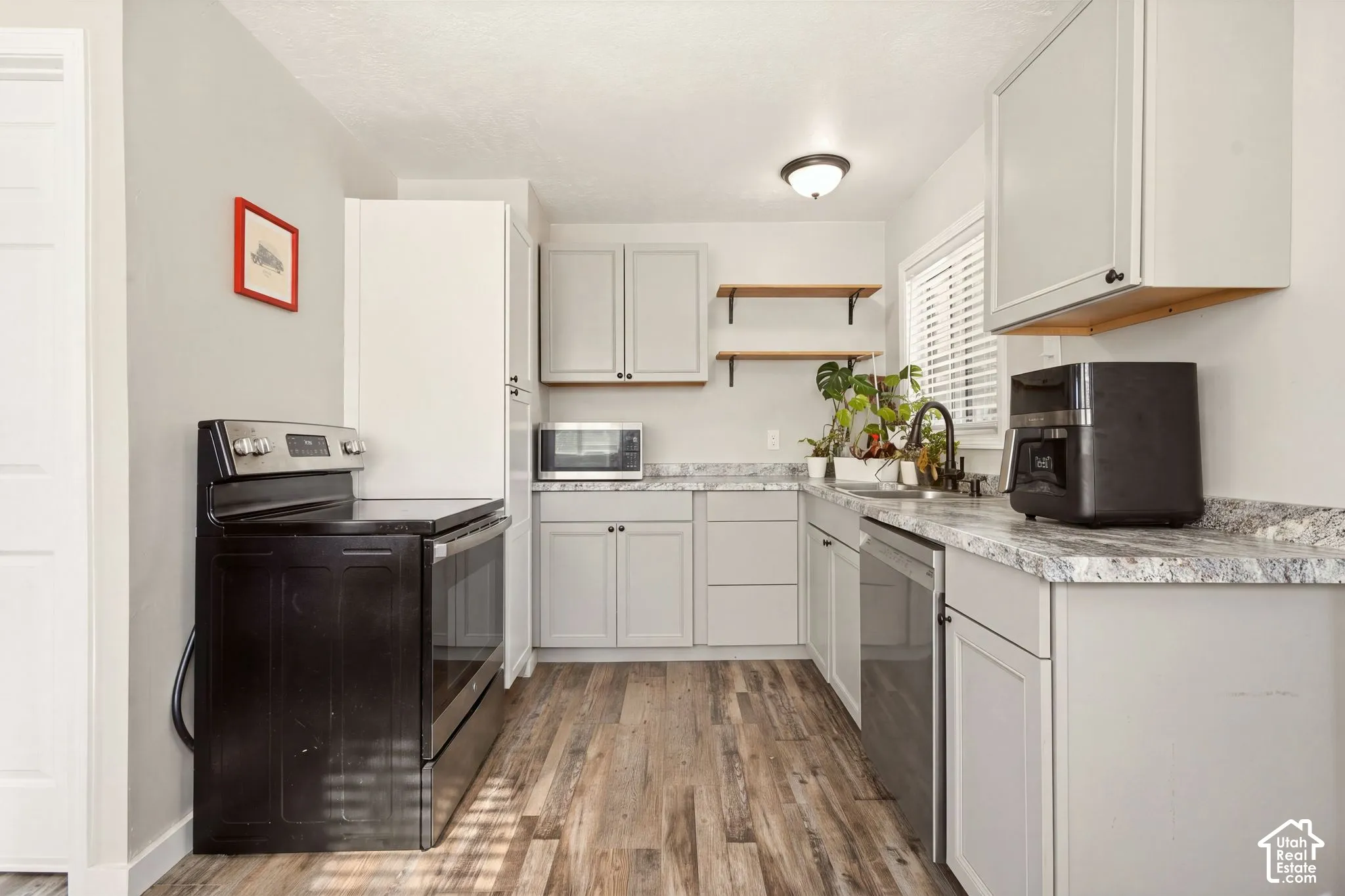 Kitchen featuring light grey cabinetry, stone-patterned countertops, wood-finish flooring, floating wood shelving, and stainless steel appliances