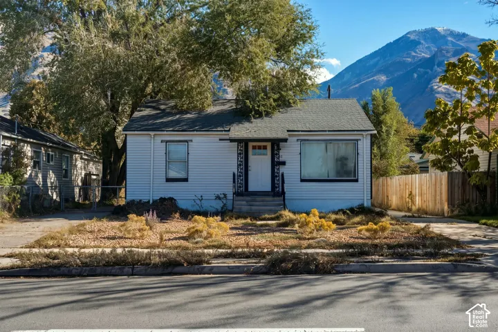 Single-story home featuring light-colored siding, a gabled roof, an entrance with an overhead canopy, and xeriscaped front grounds against a mountain backdrop