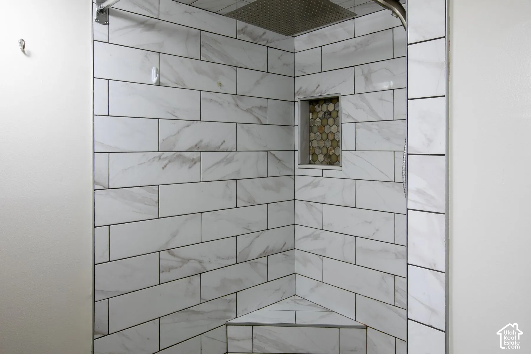 Shower enclosure featuring large-format rectangular wall tile with a veined pattern, built-in corner bench, recessed hexagonal tile niche, and a ceiling-mounted rainfall shower head