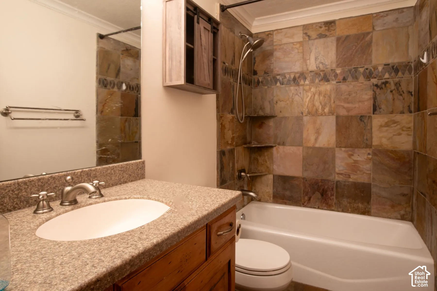 Bathroom featuring a vanity with stone-finish countertop, undermount sink, multi-tonal square tile tub surround, built-in wall cabinetry, and brushed nickel hardware