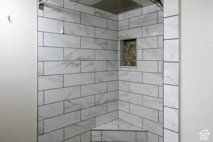 Shower enclosure featuring large-format rectangular wall tile with a veined pattern, built-in corner bench, recessed hexagonal tile niche, and a ceiling-mounted rainfall shower head