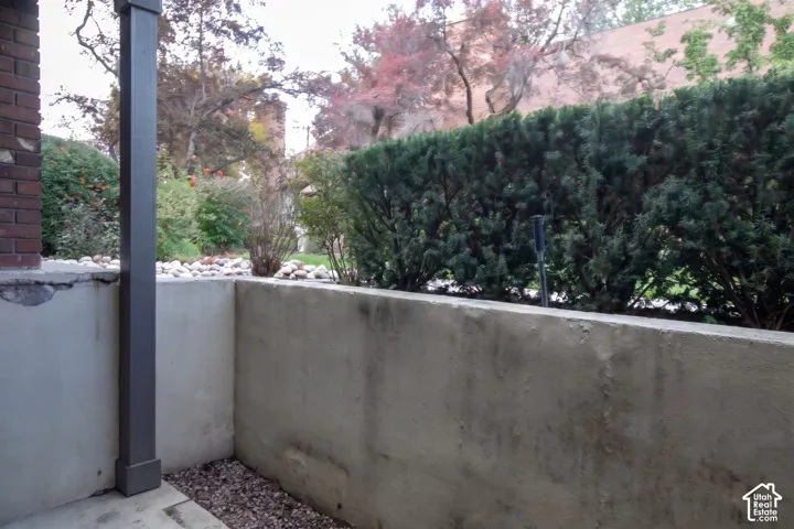 Concrete patio with a brick column, perimeter stone ground cover, and mature evergreen hedge