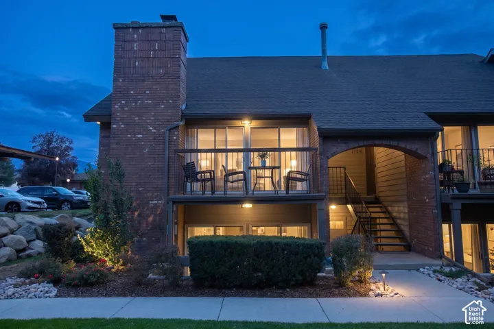 Brick exterior featuring a multi-story layout, a prominent chimney, an elevated balcony with railing, and a stone-accented landscape