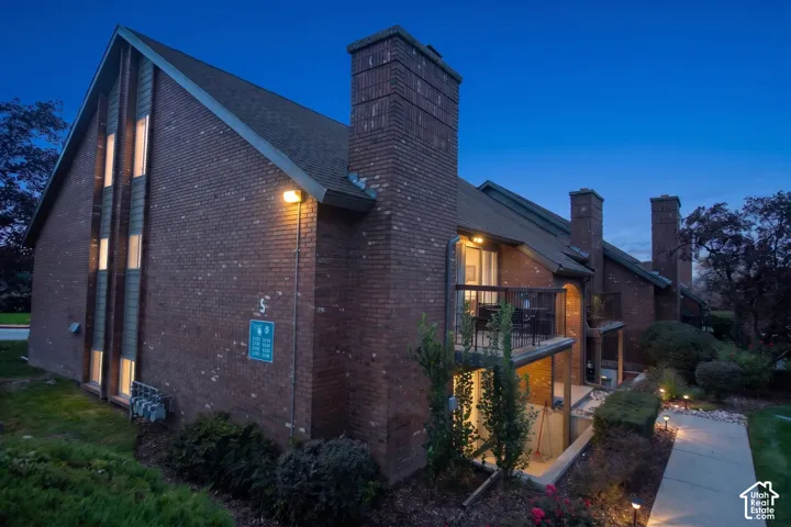 Multi-story brick exterior featuring steep roof lines, dual masonry chimneys, vertical window detailing, and elevated balconies with metal railings