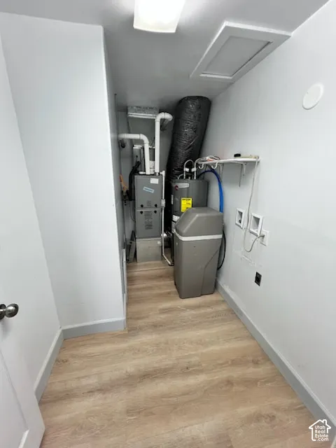 Utility space featuring wood-finish flooring, a furnace, a water heater, a water softener, and wall-mounted shelving