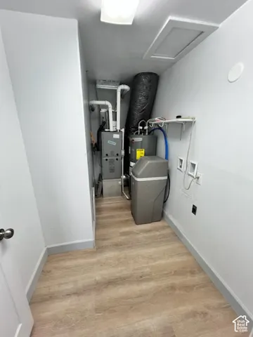 Utility space featuring wood-finish flooring, a furnace, a water heater, a water softener, and wall-mounted shelving
