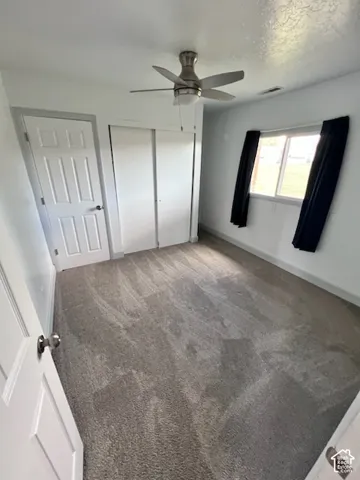 Room featuring neutral-toned carpeting, sliding closet doors, a brushed-nickel ceiling fan, and a single-hung window
