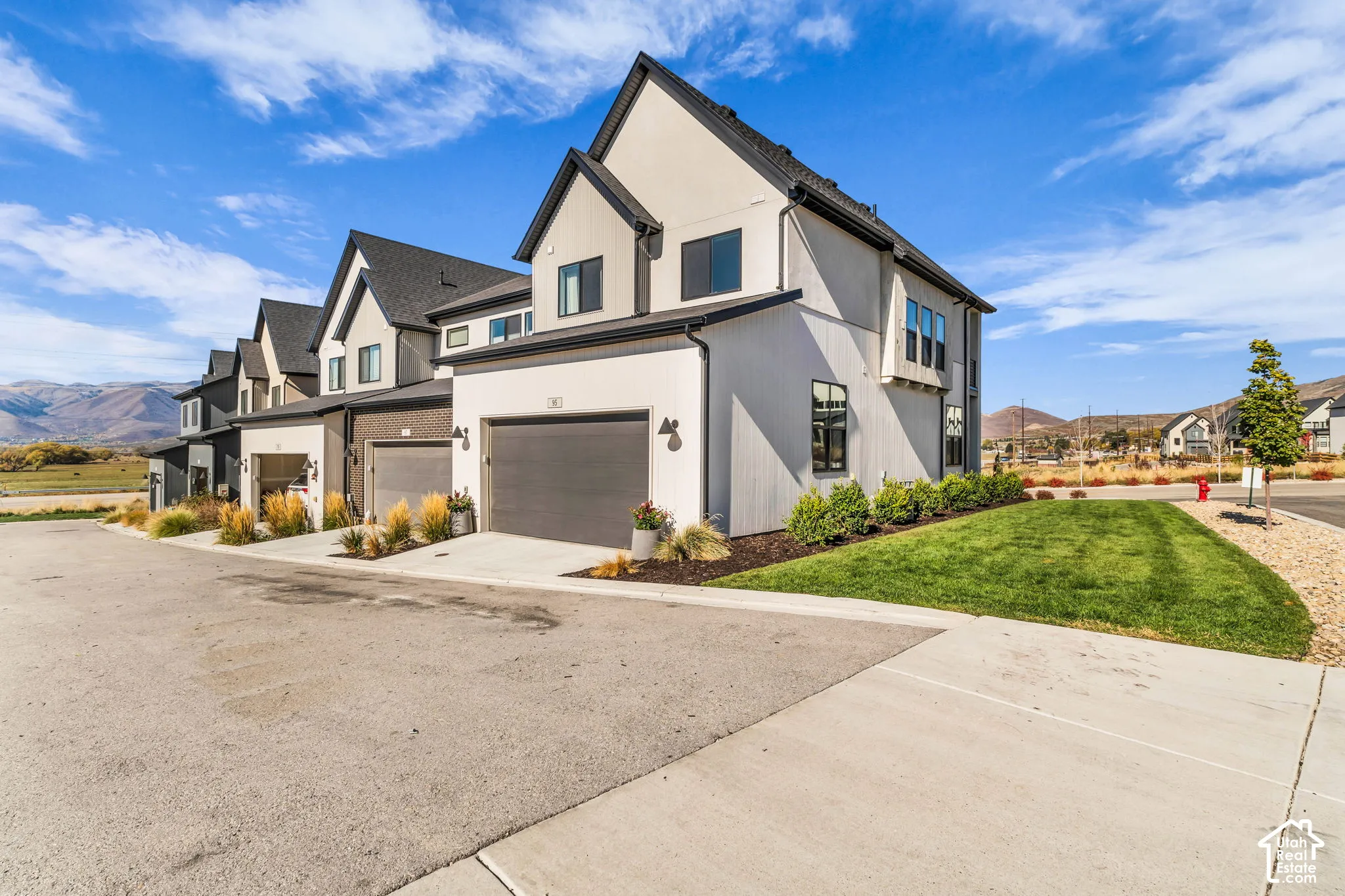 Multi-level exterior featuring vertical siding, gabled rooflines, attached garage, and landscaped lawn with mountain backdrop