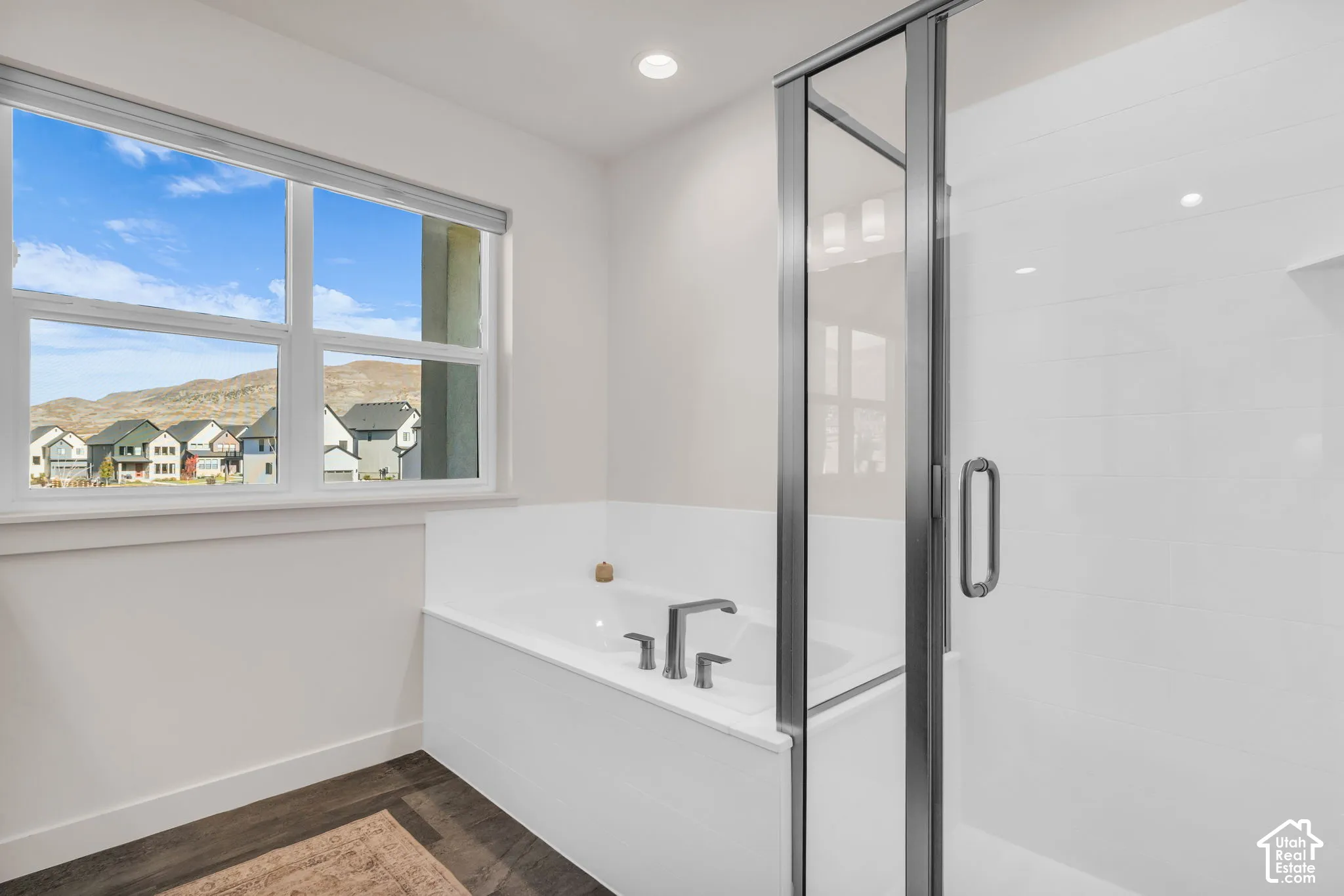 Soaking tub with deck-mounted faucet, walk-in shower with metal-framed glass enclosure, and large windows with mountain scenery