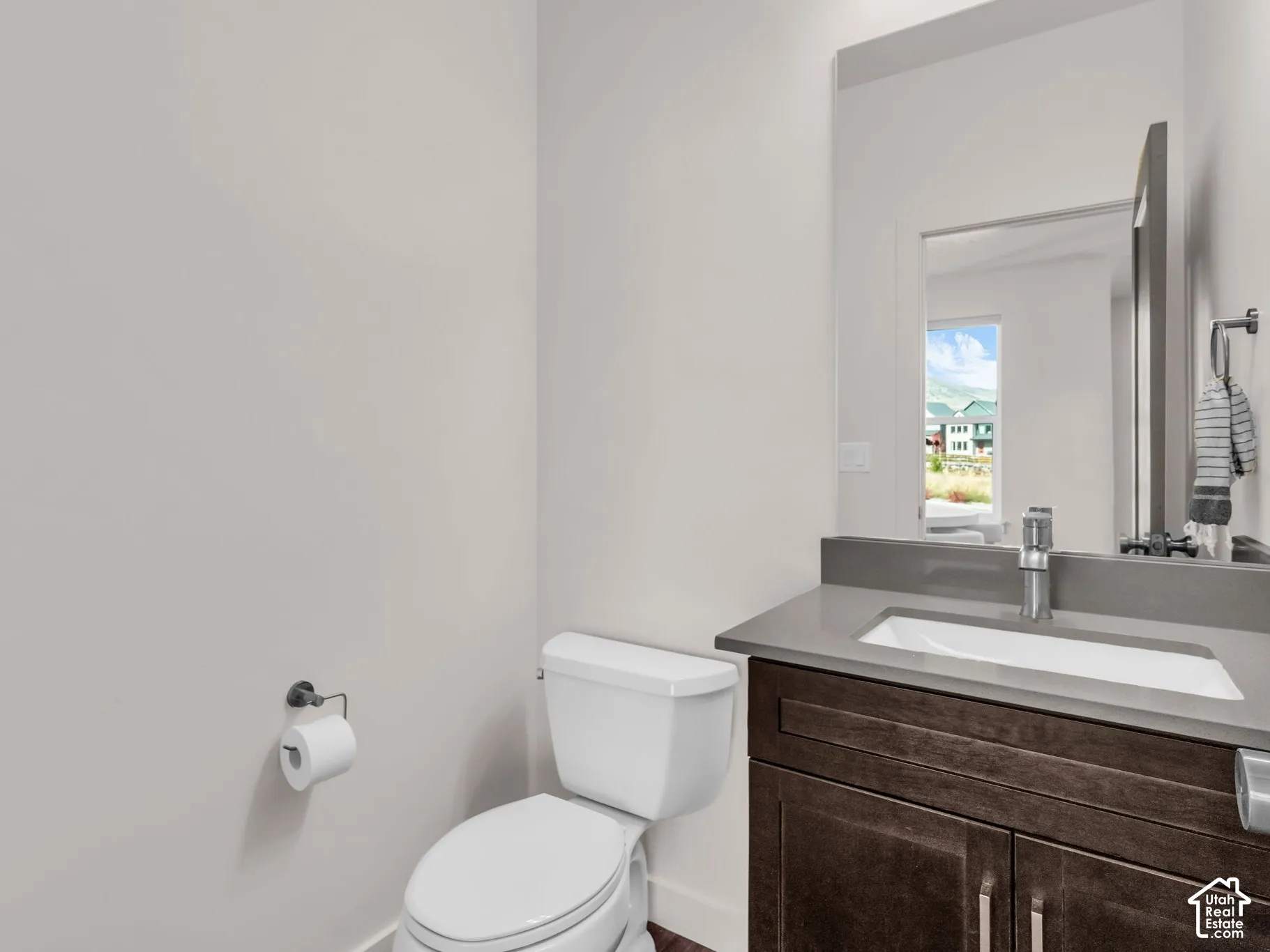 Dark wood-finish vanity with a rectangular sink, stone-composite countertop, tall mirror, and chrome faucet hardware