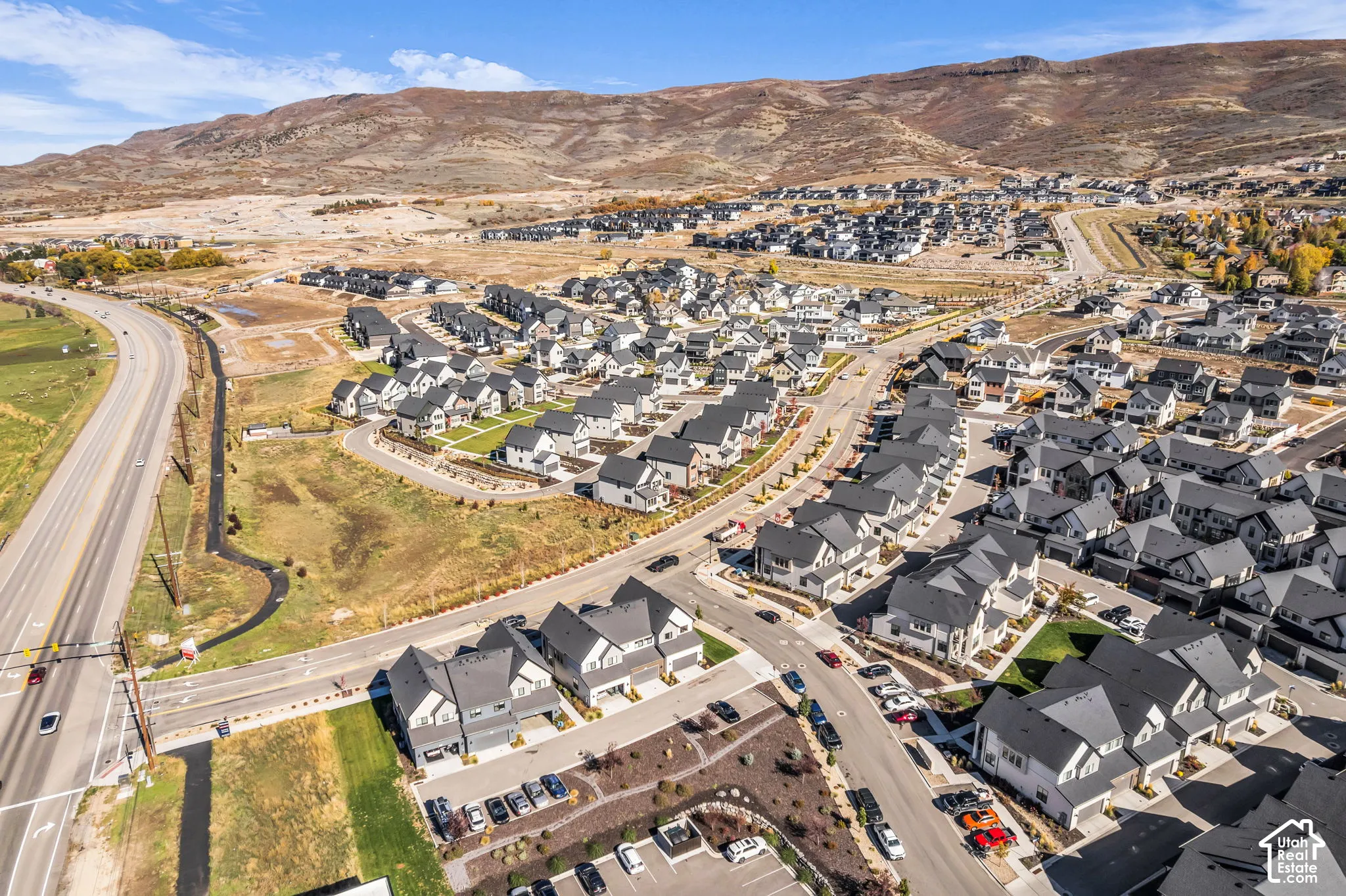 Aerial perspective of a planned community featuring multi-level residential structures, paved roadways, professional landscaping, and a mountain backdrop