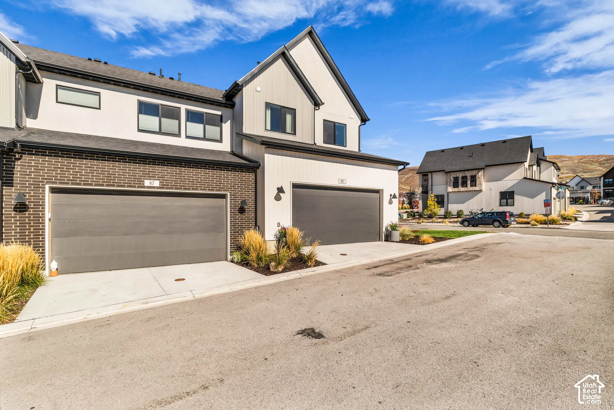 Contemporary multi-level exterior featuring a combination of dark brick veneer and vertical panel siding, dual-car garages, and steep roof pitches