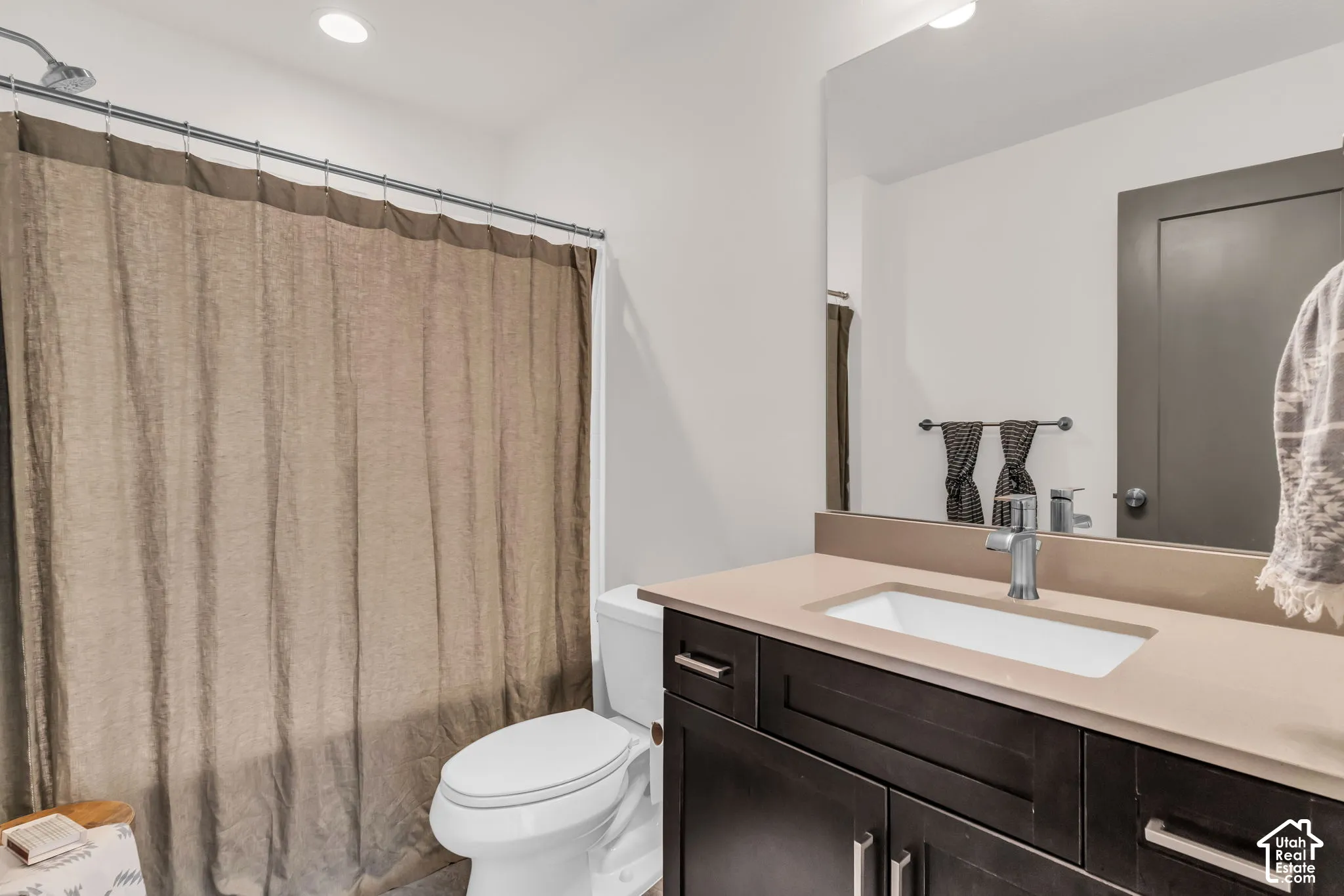 Bathroom featuring a vanity with dark wood-finish cabinetry, a solid surface countertop, an integrated rectangular sink, a large wall-mounted mirror, and a shower-tub combination