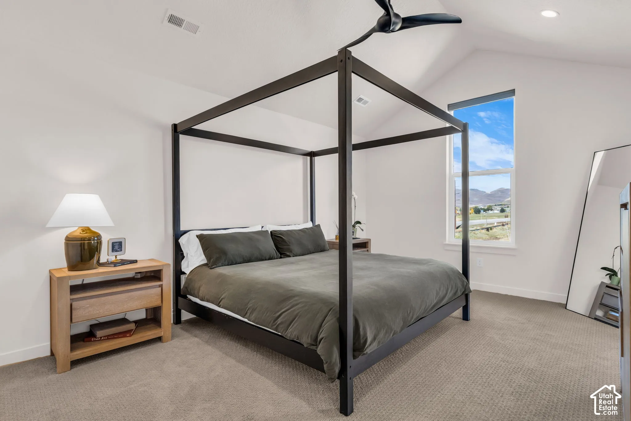 Vaulted ceiling featuring a central matte black ceiling fan, neutral carpeting, and a large vertical window with a mountain backdrop