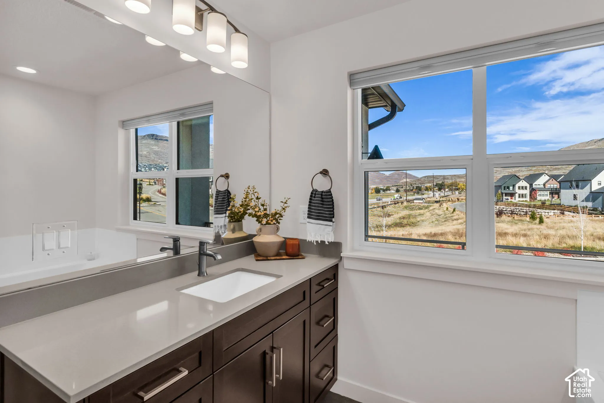 Dark-finish cabinetry paired with a light-toned solid surface countertop, rectangular undermount sink, matte finish faucet, and full-width wall mirror