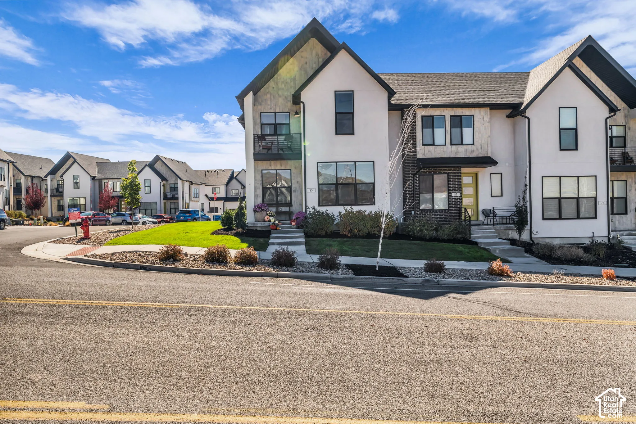Multi-level townhouse exterior featuring a white stucco facade with stone masonry accents, dark-framed windows, steep gabled rooflines, and a private balcony