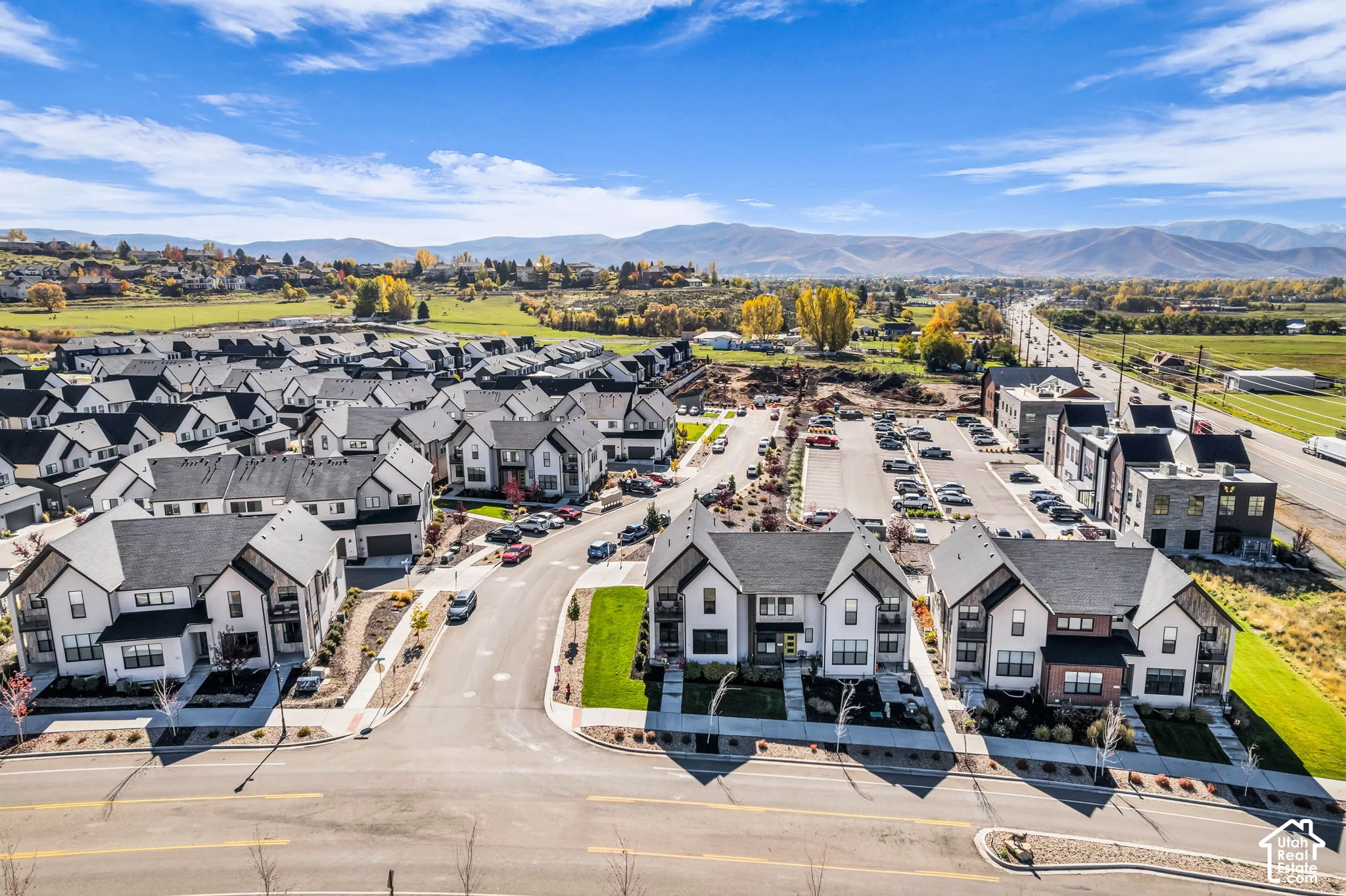 Aerial perspective of a multi-unit residential community featuring modern architectural facades, dark pitched roofs, paved internal streets, and a mountainous backdrop