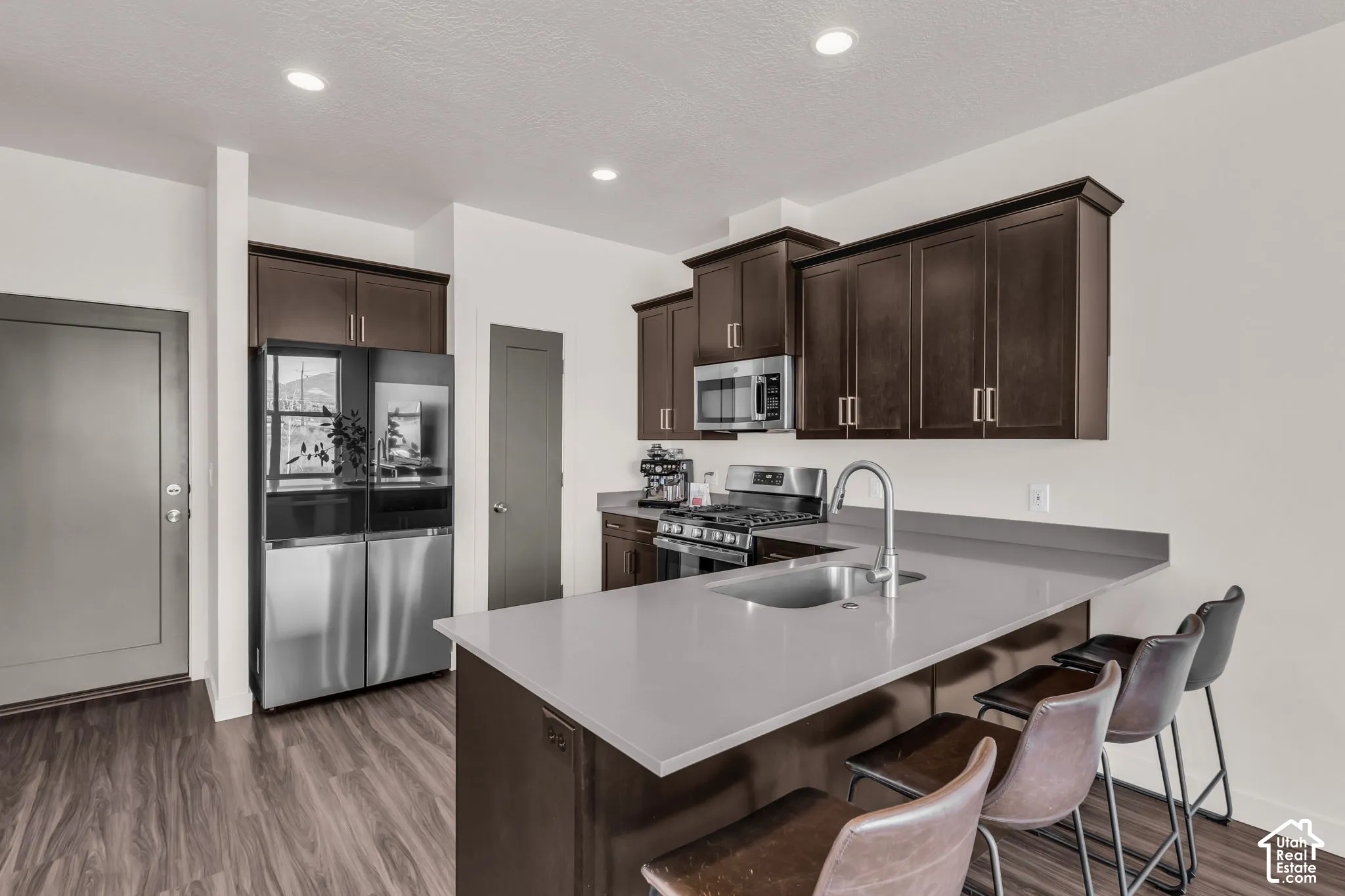 Kitchen featuring dark wood-finish cabinetry, quartz countertops, a stainless steel undermount sink, integrated stainless steel appliances, and wood-finish flooring