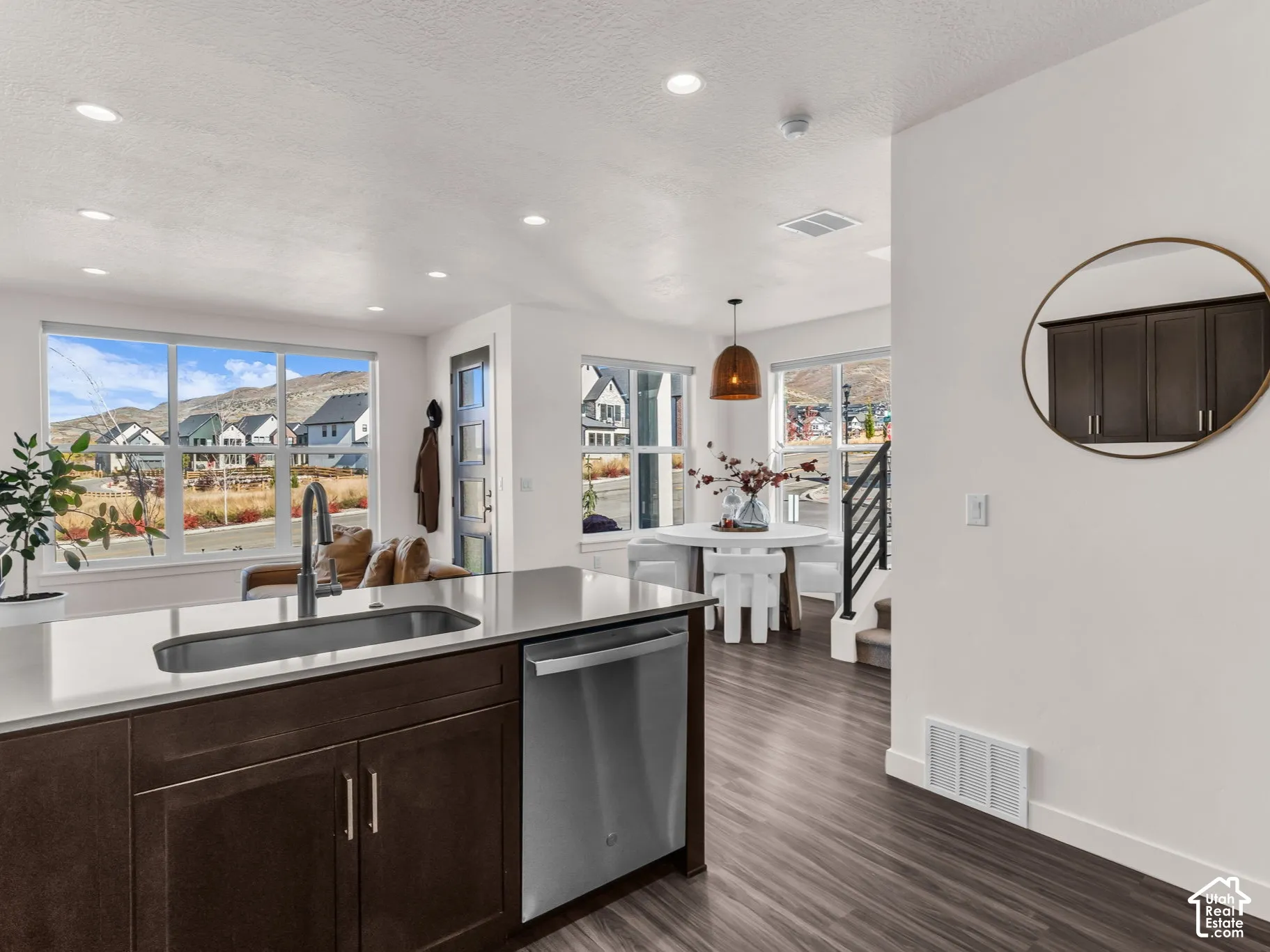 Kitchen island featuring dark wood-finish cabinetry, a light-toned solid surface countertop, an undermount sink with a gooseneck faucet, and a stainless steel dishwasher