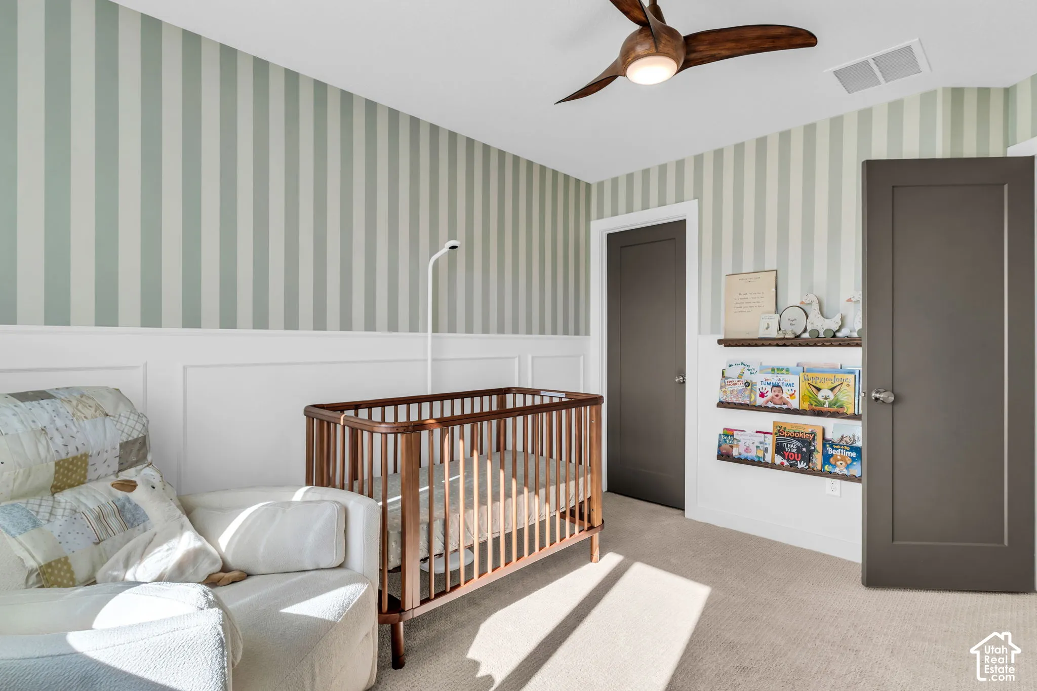 Room featuring half-wall wainscoting, vertical striped wallpaper, integrated wood-finish ceiling fan with light fixture, neutral carpeting, and dark-toned solid-core interior doors