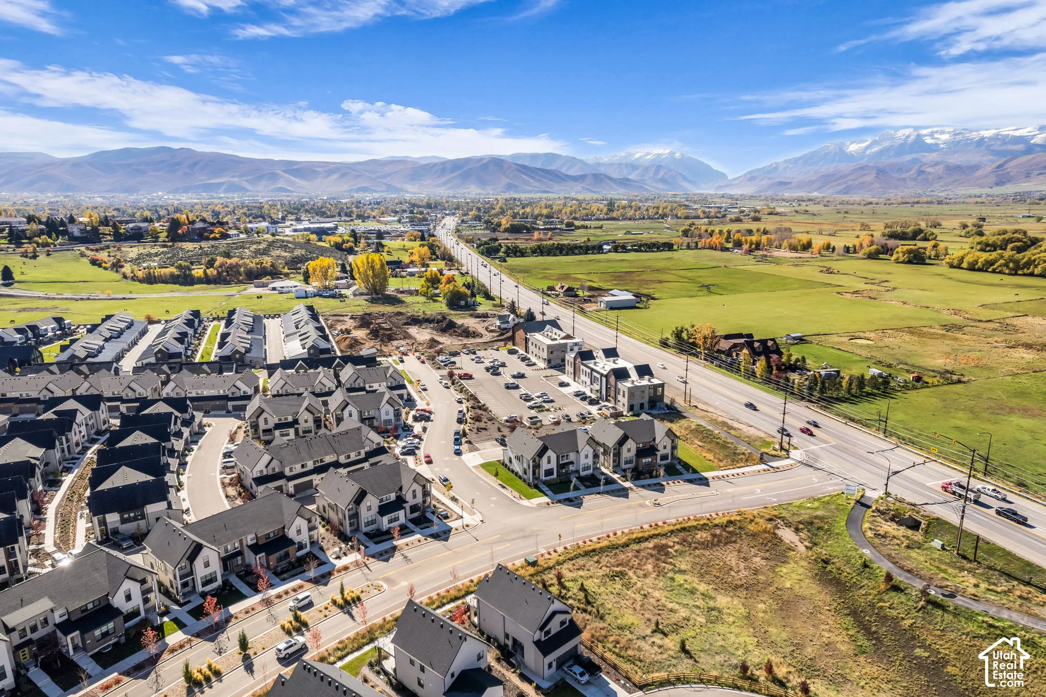 Aerial perspective of residential community featuring multi-story structures with pitched roofs, paved internal roadways, integrated parking areas, and a mountain range backdrop