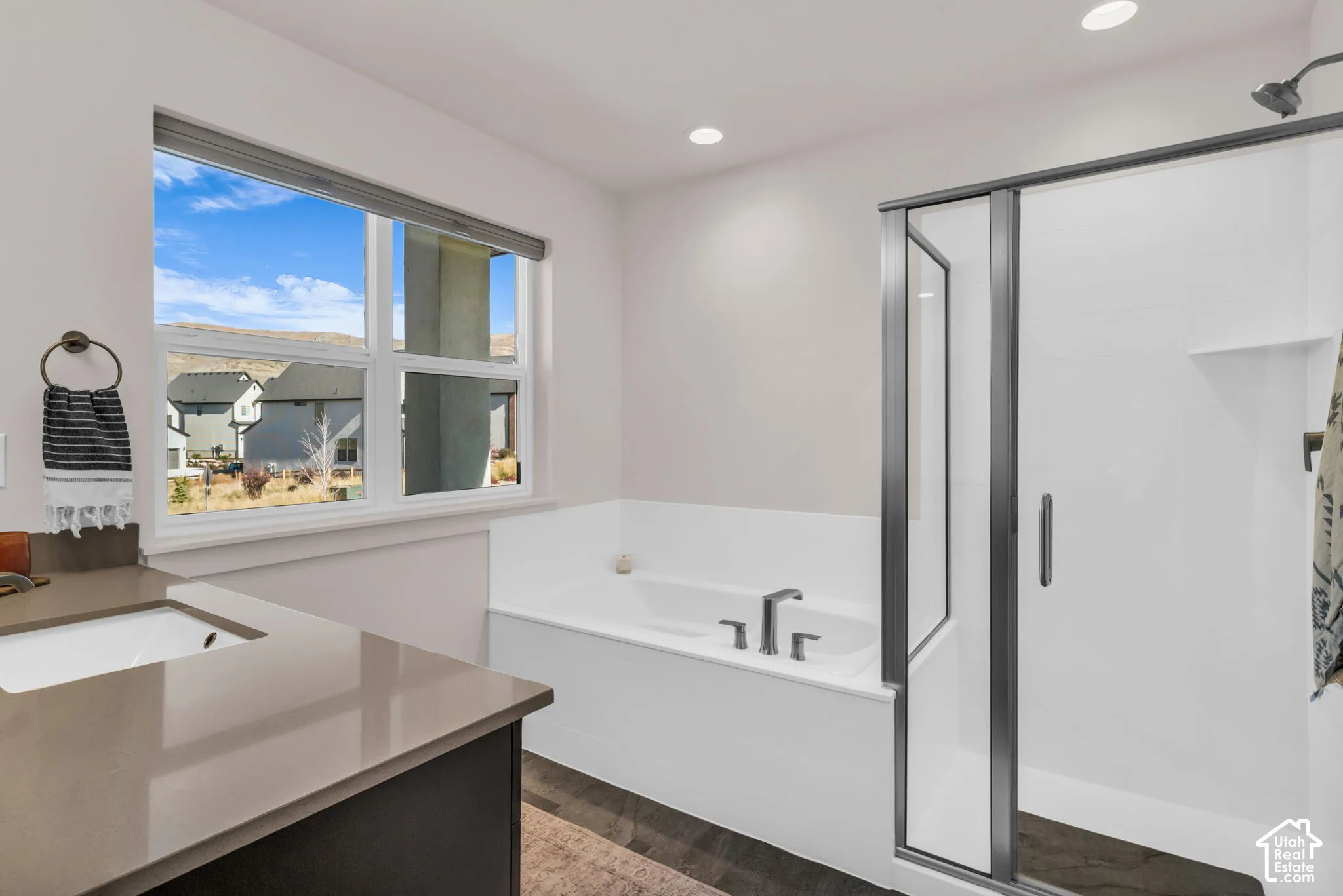 Bathroom featuring a solid-surface countertop with an integrated sink, a deep soaking tub, a glass-enclosed shower with metallic hardware, and recessed lighting