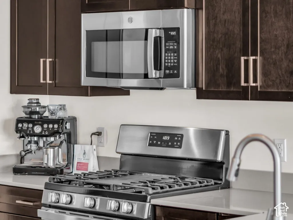Dark wood cabinetry featuring crown molding, stainless steel microwave, gas range, solid surface countertops, and an undermount sink