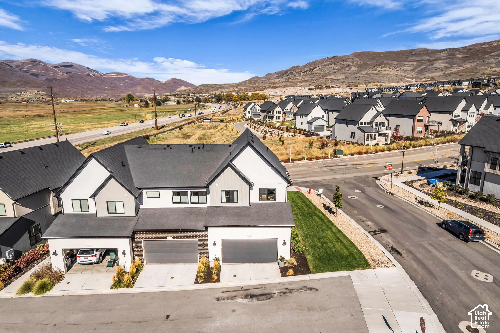 Multi-level residence featuring a composite shingle roof, painted masonry and horizontal siding exterior, dual attached garages, and mountain backdrop