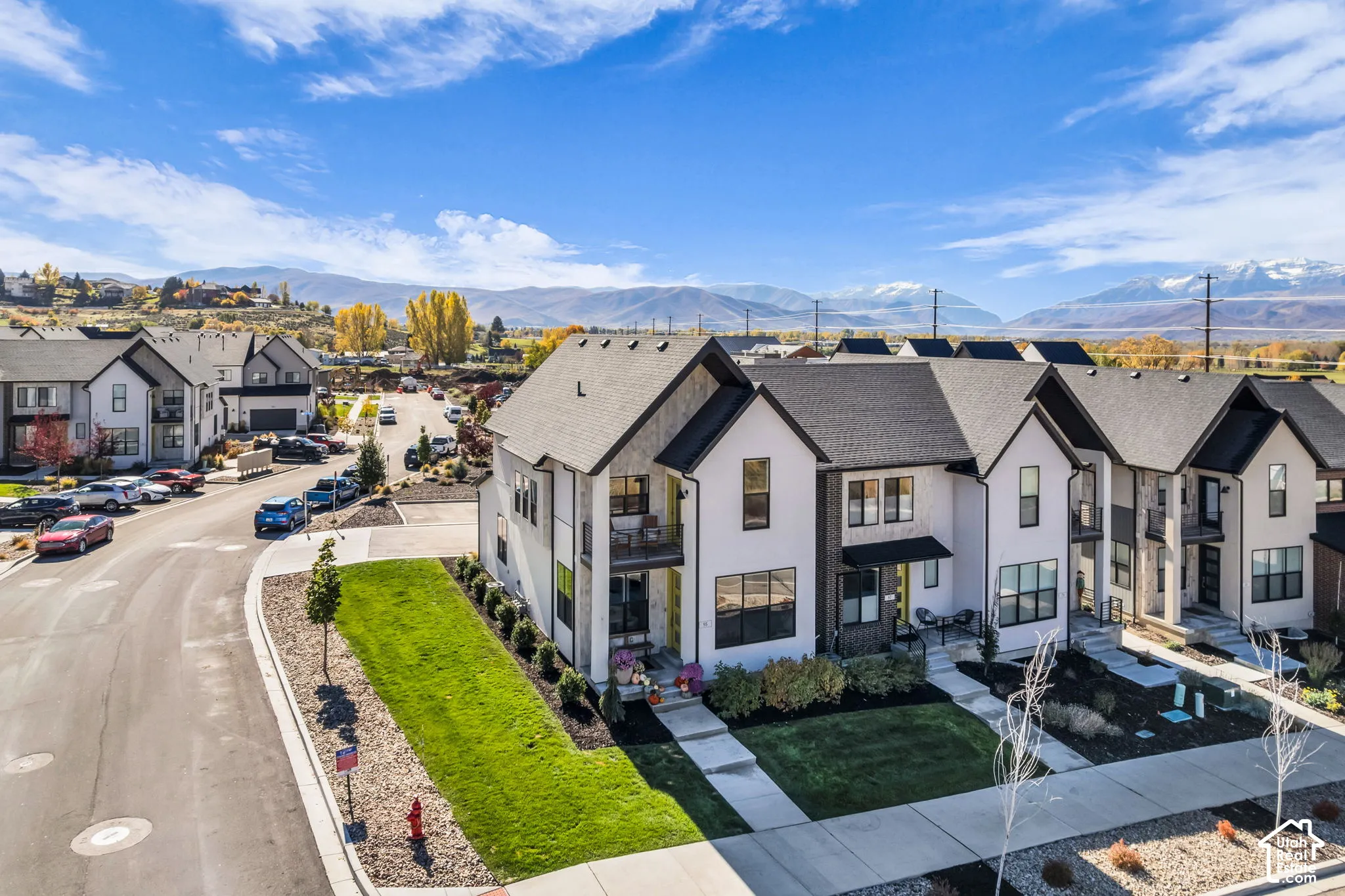 Modern multi-story townhome exterior featuring high-contrast white and dark brick facade, covered balcony, shingle roof, and mountain backdrop