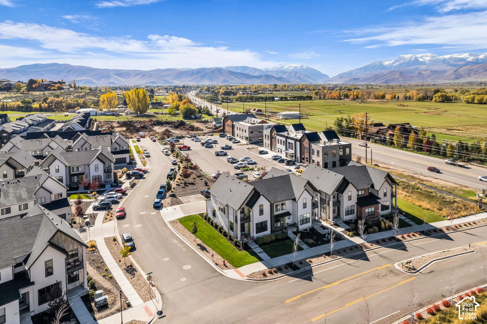 Aerial perspective of multi-family residences featuring architectural gables, high-contrast exterior finishes, paved street infrastructure, and mountainous horizon