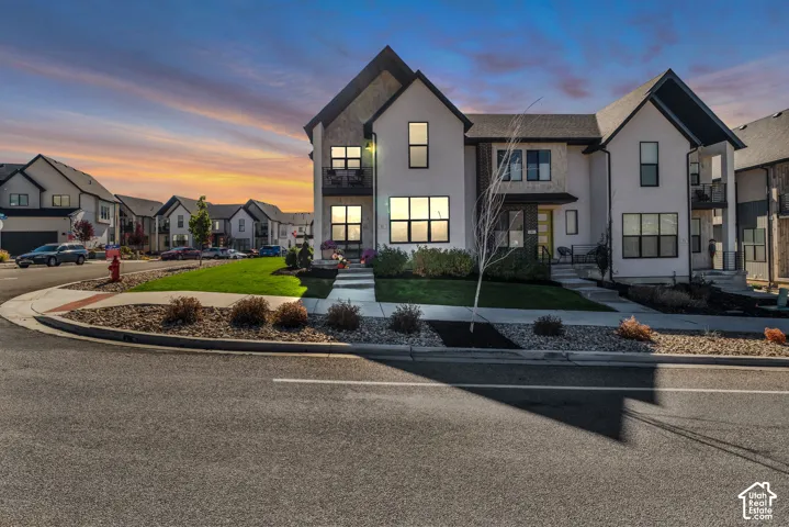 Modern multi-story exterior featuring a mix of stucco and stone siding, gabled rooflines, large rectangular windows, and a private balcony
