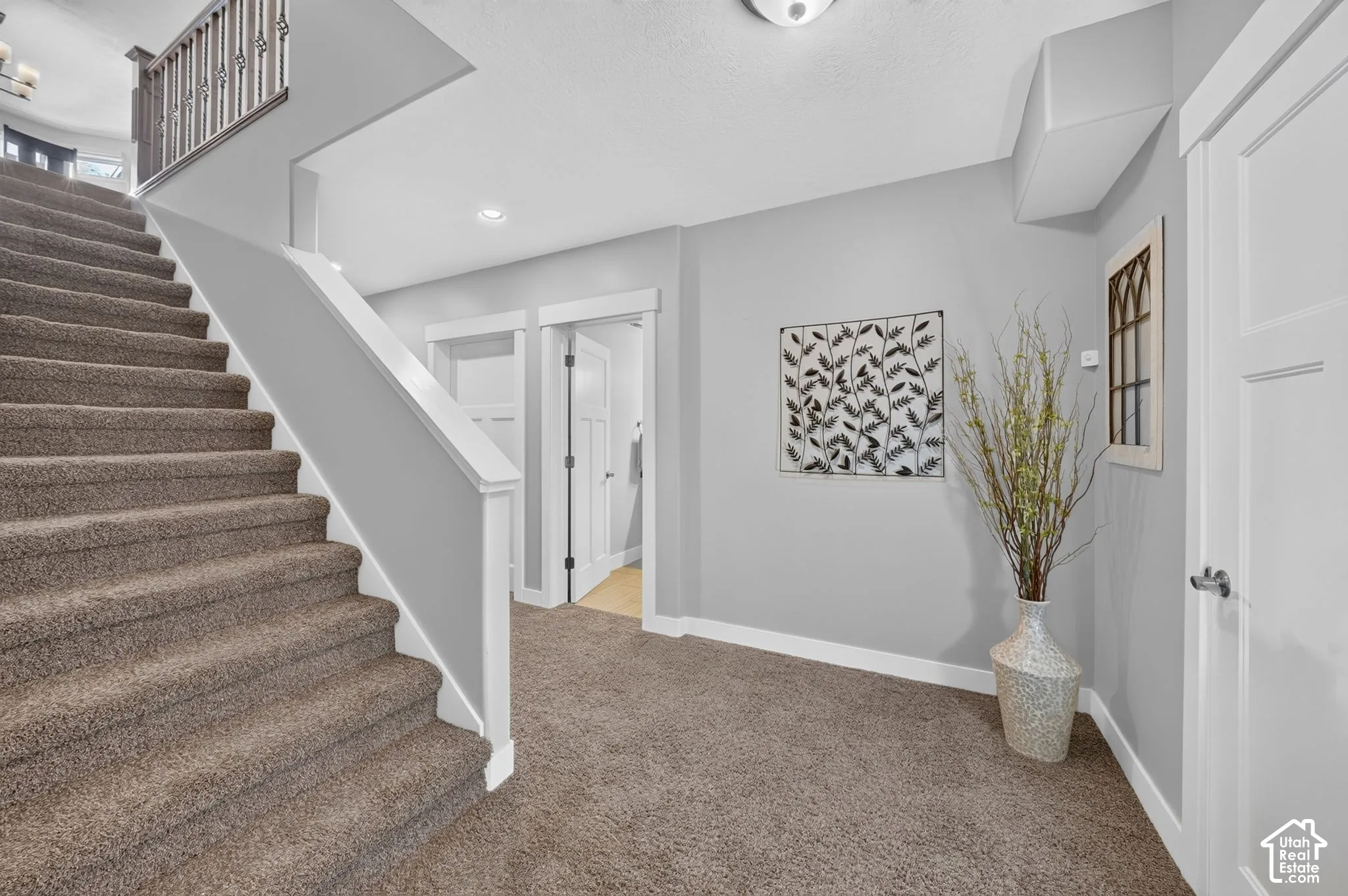 Carpeted staircase featuring a metal-spindle railing, neutral wall color, recessed lighting, and interior doors with craftsman-style trim