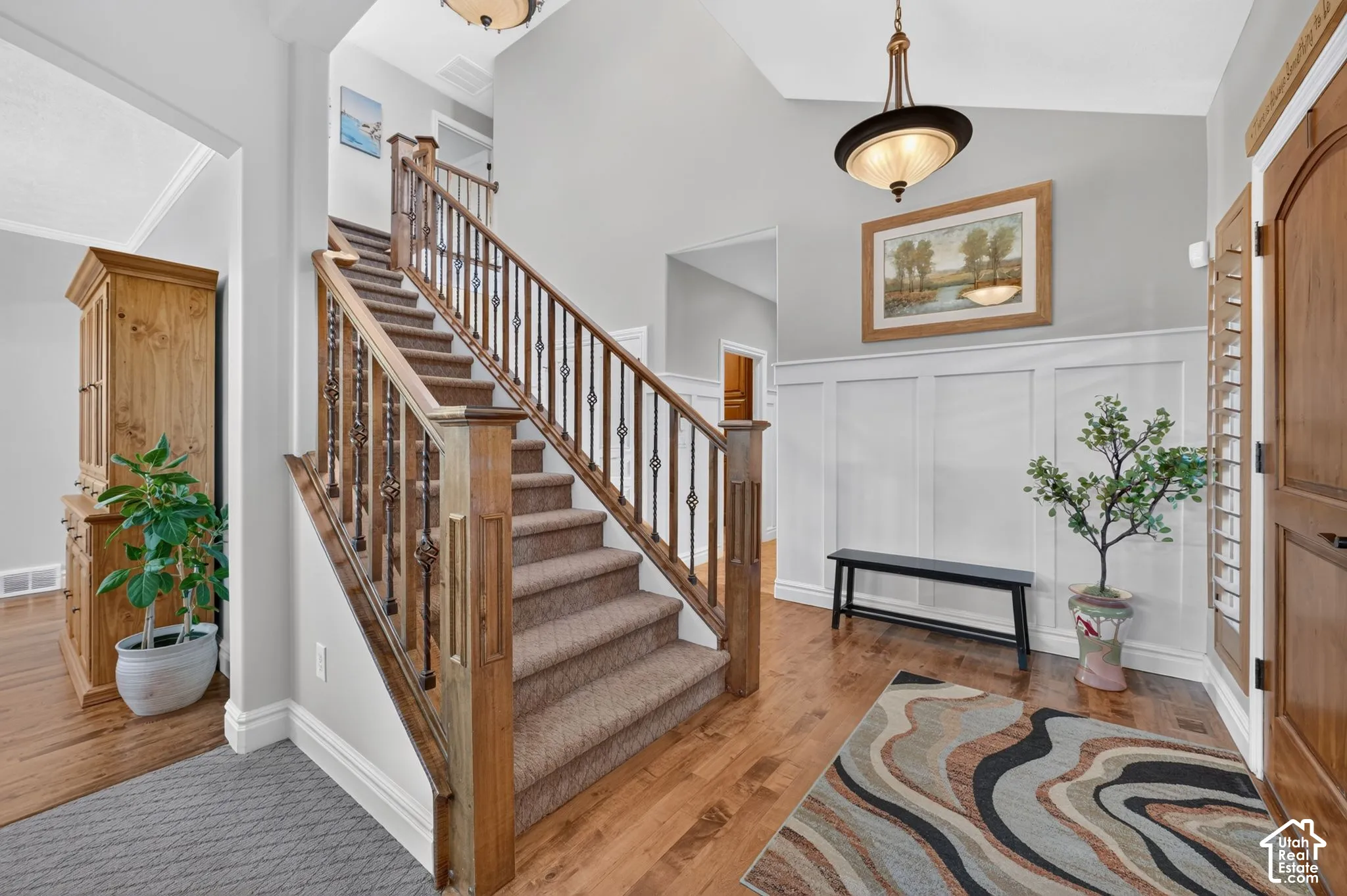 Foyer featuring vaulted ceilings, wood-finish flooring, wainscoting, and a staircase with stained wood railings and metal balusters
