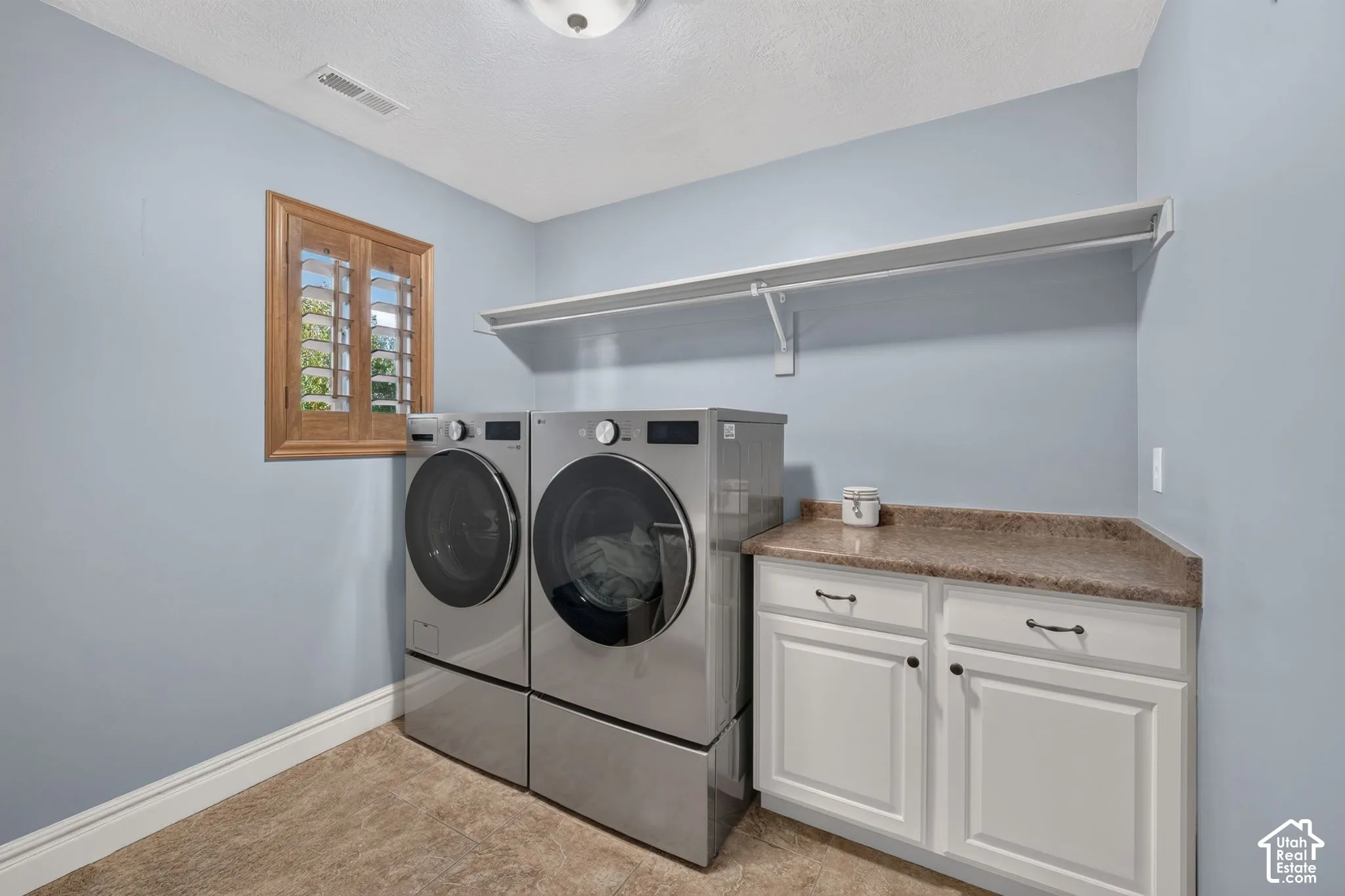Laundry room featuring white cabinetry, stone-finish countertop, full-width wall shelving, and plantation-style window shutter