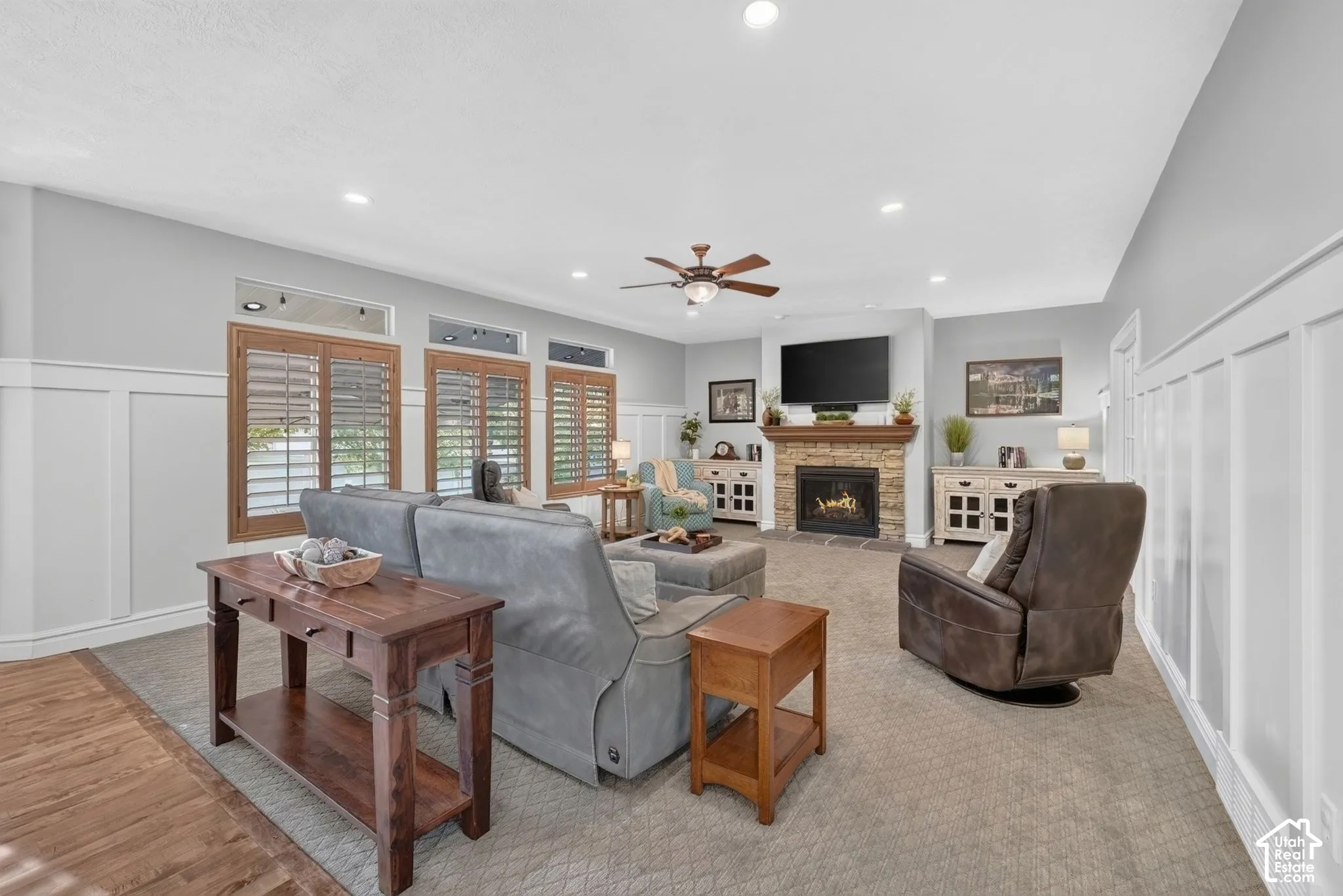 Living area featuring a floor-to-ceiling stone-faced fireplace, white wainscoting, recessed lighting, and wooden interior shutters